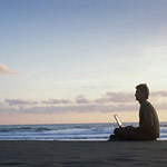 Image of a man on a beach looking at a laptop computer