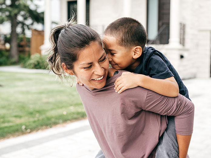 A mother carrying her child on her back with a joyful smile on her face
