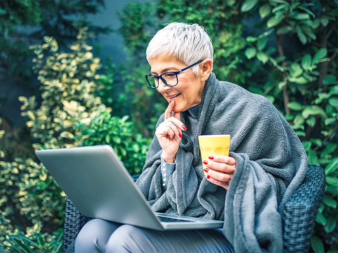 a woman holding a coffee looking at her laptop