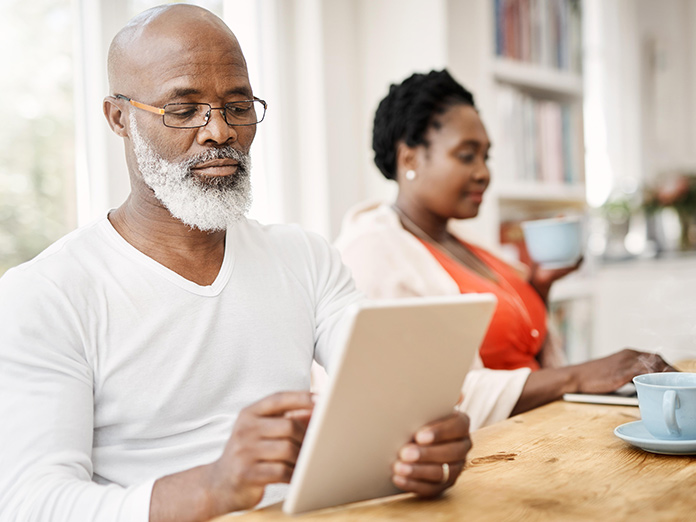 Two people sitting at their kitchen table, one of them with Medicare mail order pharmacy benefits.