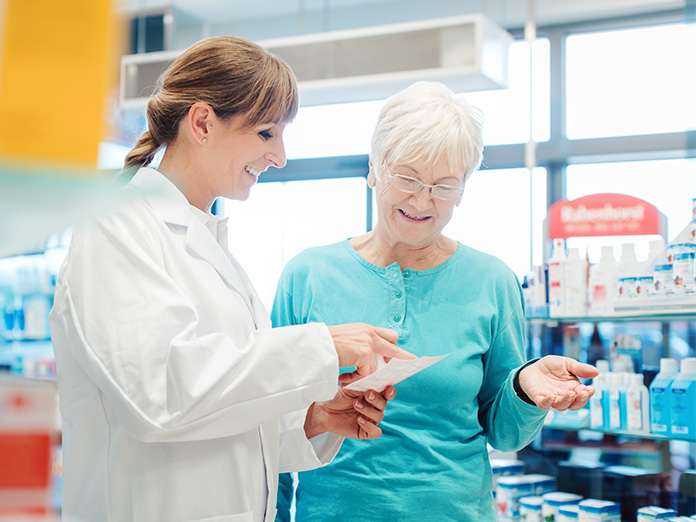 A pharmacist in a retail pharmacy setting reviews prescription information with an older adult.