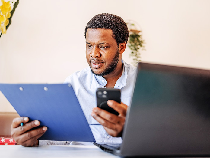 Man Looking at Clipboard While Holding Phone