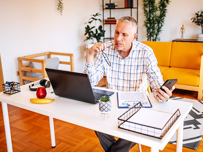 Man Looking at Laptop While Holding Phone