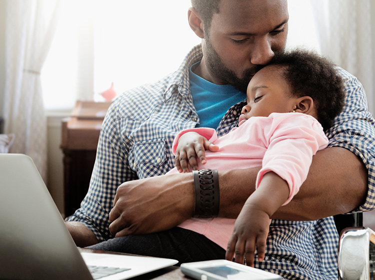 Padre joven usa la computadora con su hija dormida en brazos