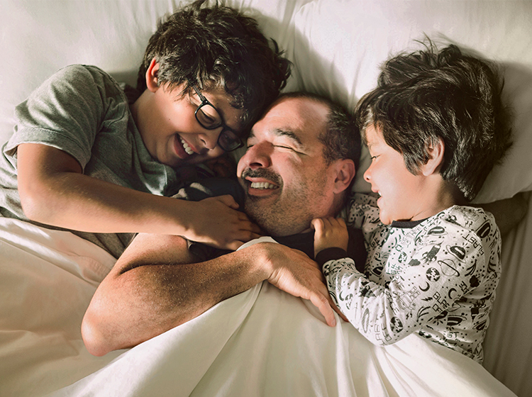 Sons tickling and laughing with their father on bed